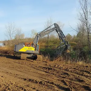Excavator with a grapple attachment pulling woody growth off the top bank