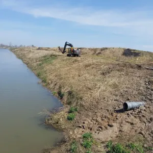 Cleared ditch reach with an excavator working the top bank and culvert pipe staged alongside