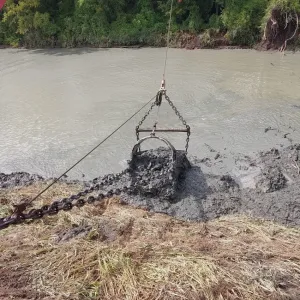 Bucket of excavated channel material lifted clear of the water