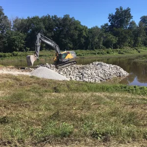 Excavator placing crushed stone and riprap to build the cofferdam across the channel