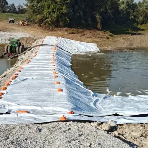 Geotextile-lined cofferdam sealed with sandbags, with a tractor-mounted pump unwatering the work area