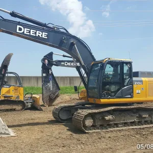 Tracked excavator fitted with a hydraulic shear staged near the floodwall, with a crawler dozer parked behind