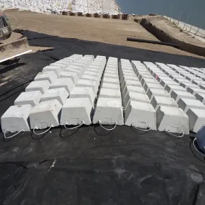 Single rows of concrete blocks with lifting cables laid out on geotextile, sheet piling and water visible beyond