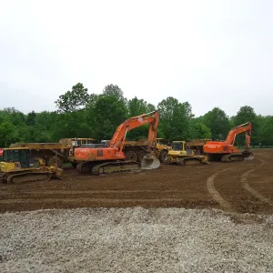 Row of idle equipment parked on a graded pad — dozers, articulated dump trucks and two excavators