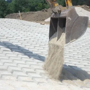 Excavator bucket dumping fine aggregate onto placed articulated concrete block revetment