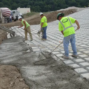 Crew placing and vibrating concrete along the toe of the block revetment with a mixer truck discharging from the bench above