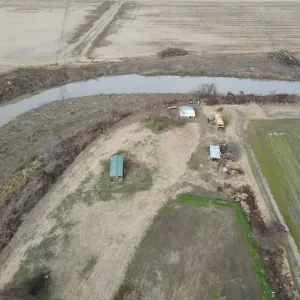 Cleared brush and timber stacked along the top bank at a channel bend, ahead of excavation