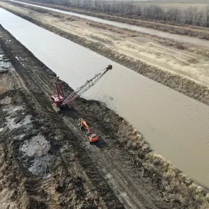 Dragline casting excavated material out of the channel while an excavator dresses the spoil