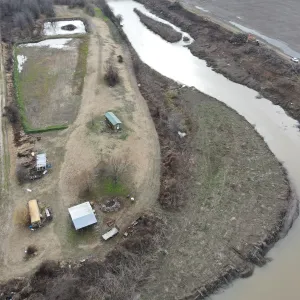 Long-reach excavator working the far top bank opposite private property on a channel bend