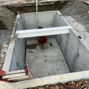 Precast concrete vault set in an excavation, containing a flanged blind-flange riser and a steel beam spanning the vault walls