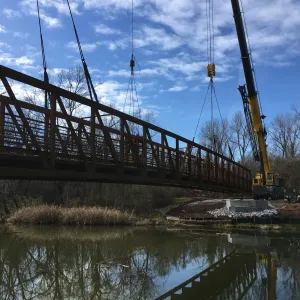 The prefabricated span suspended on crane rigging beside the completed abutment
