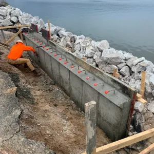 Concrete cap wall being finished along the riprap shoreline with embedded anchors in place
