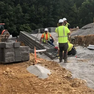 Crew setting the lower MSE block courses with drainage pipe and compacted backfill behind