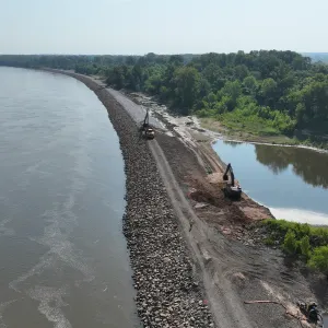 Aerial view of the crest haul road and riprap slope with an excavator working an excavated section beside the landside water