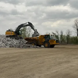 Excavator on a stone stockpile loading an articulated dump truck in the staging area