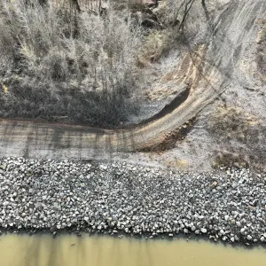 Overhead view of the riprapped bank and gravel access road with an eroded gully cut into the landside slope