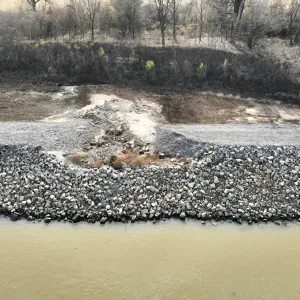 Overhead view of the riprapped bank with a washout notch cutting through the crest road and stone blanket