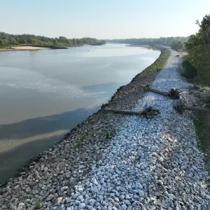 Aerial view of the finished riprap slope with fallen trees and driftwood lying across the placed stone